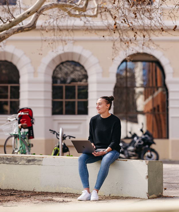 Notre Dame female student wearing a black top and blue jeans using a laptop sitting outside of Customs House on the Fremantle Campus. 